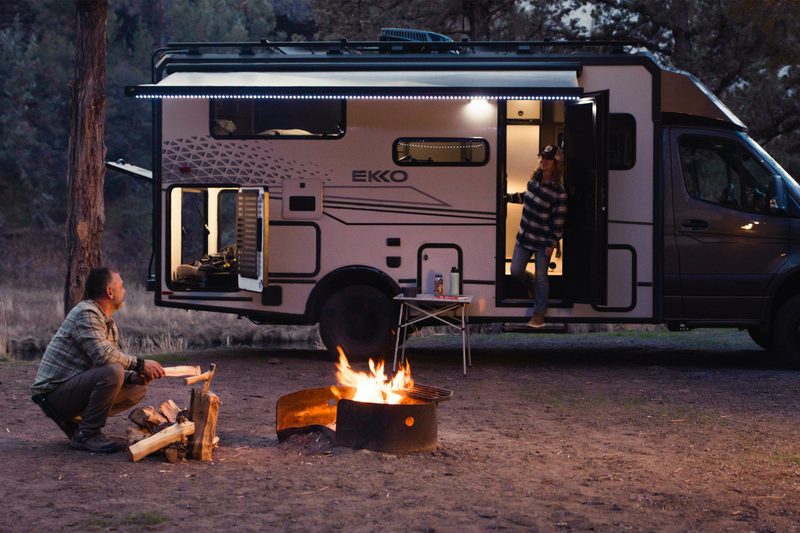 Man building a campfire in front of a Winnebago Ekko Springer camper van.