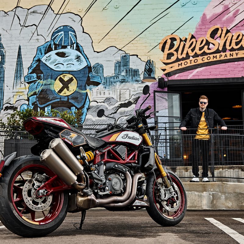 2024 Indian FTR x RSD Super Hooligan parked in front of Bike Shed store with a person leaning against metal fence looking directly at the camera.