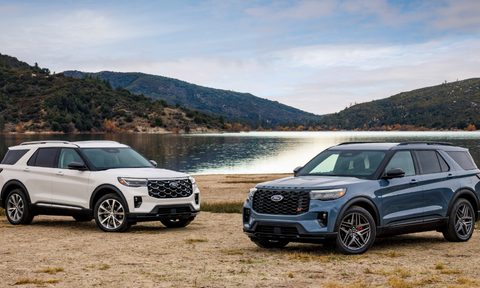 2025 Ford Explorer Platinum and 2025 Ford Explorer ST barked on stones by lakeside with moutains in the background.