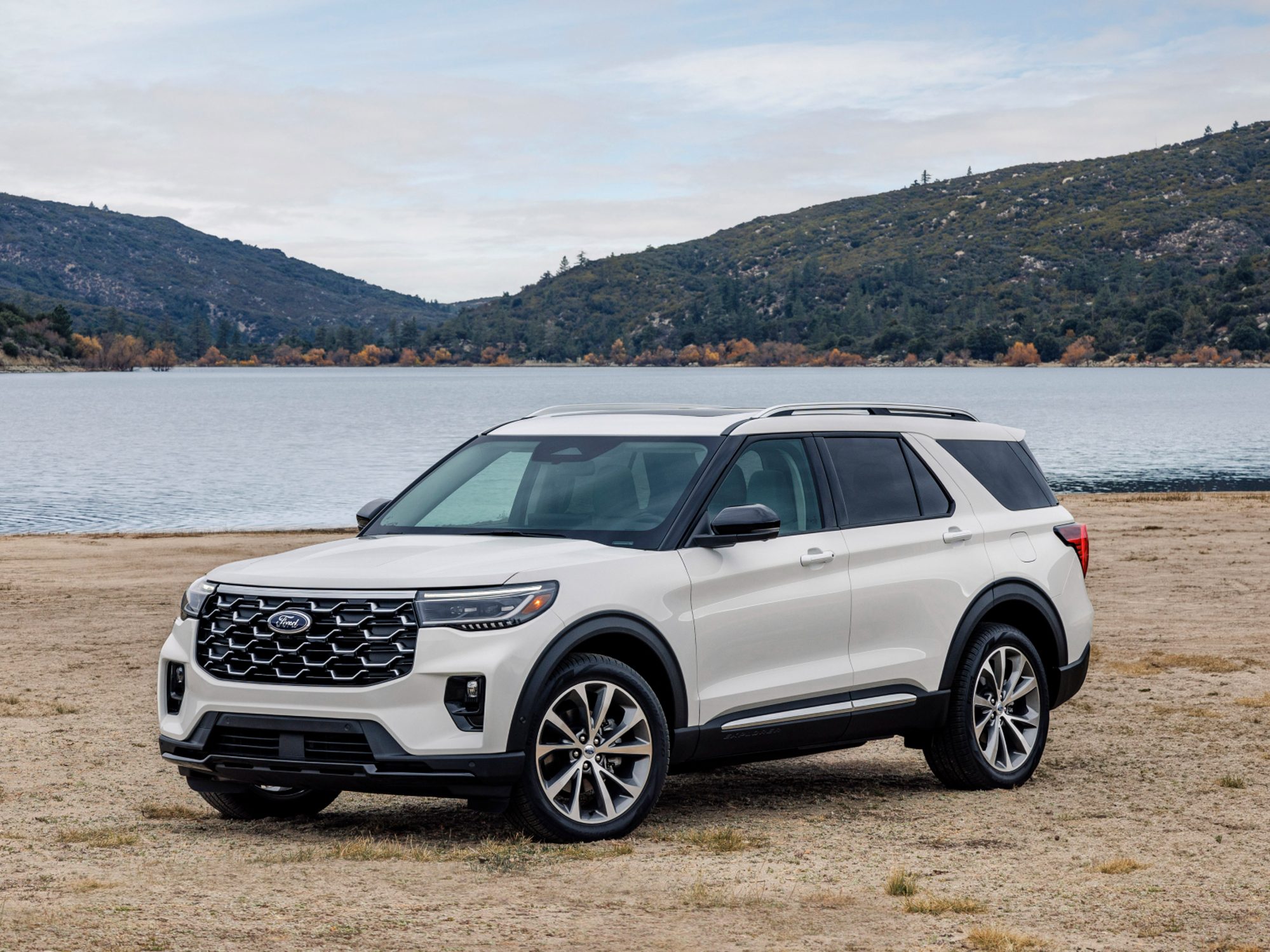 2025 Ford Explorer Platinum parked on a beach by a lake with mountains in the background.