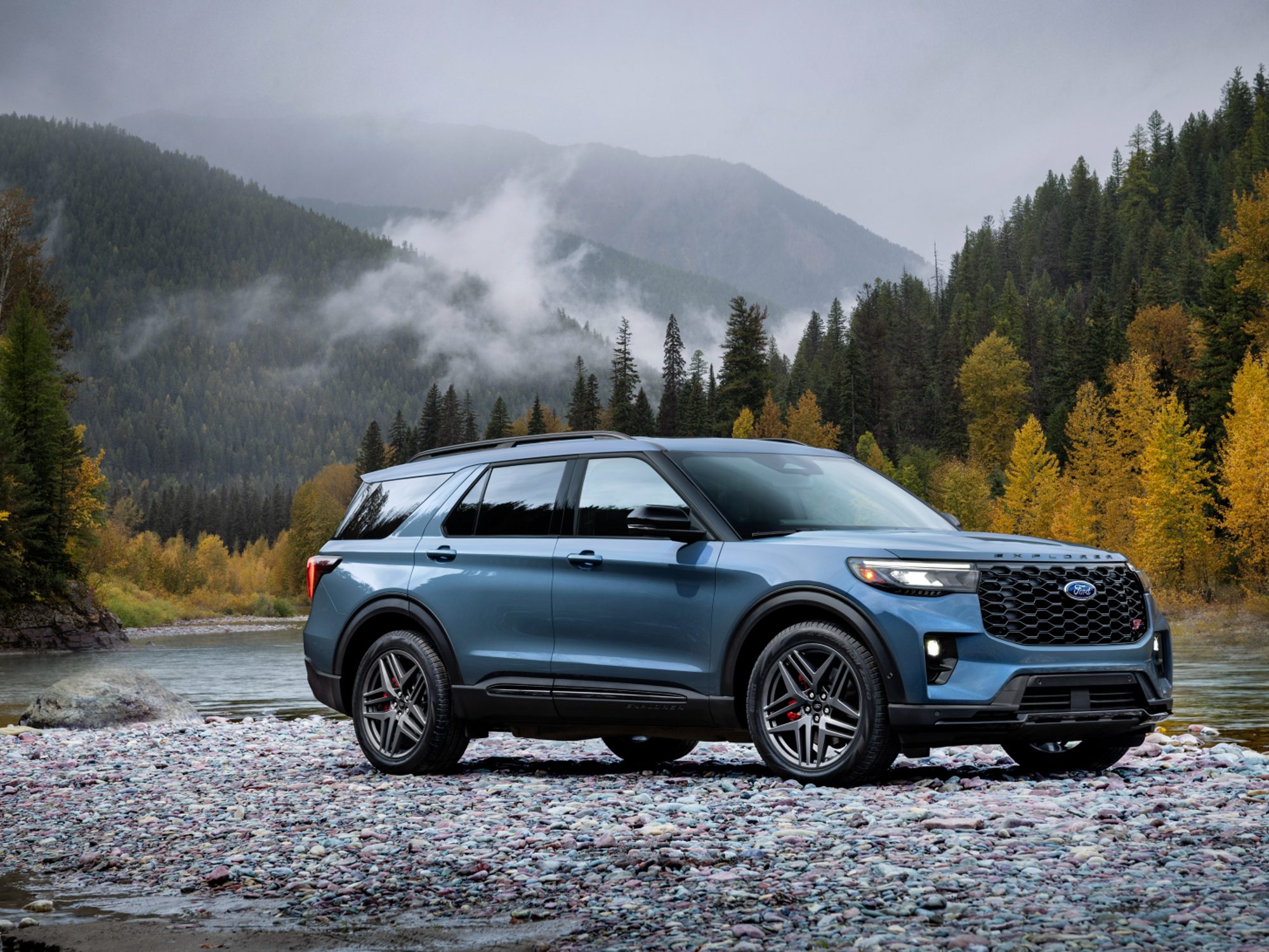 2025 Ford Explorer ST parked on stones by a lake with forested mountains in the background