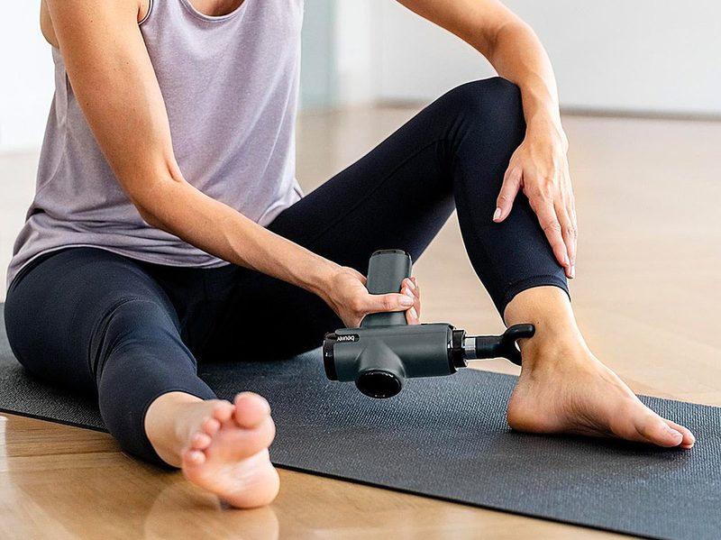 A woman uses the Beurer compact massage gun to massage her ankle.