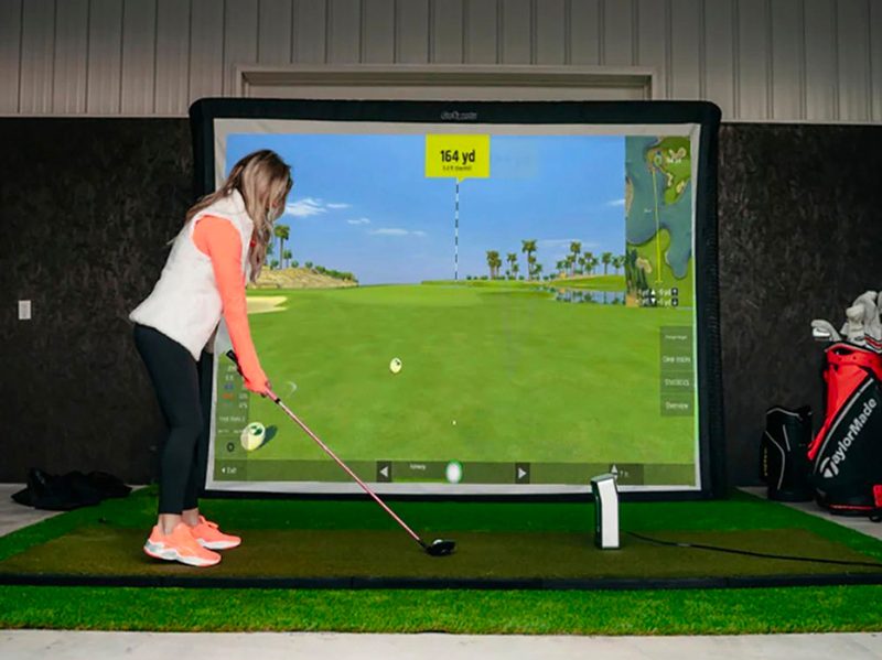 A woman prepares for a swing on the OptiShot BallFlight + Net Bundle golf simulator.