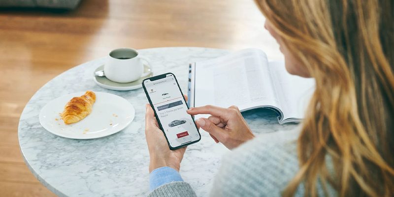 A woman using the Porsche app while sitting at a table.