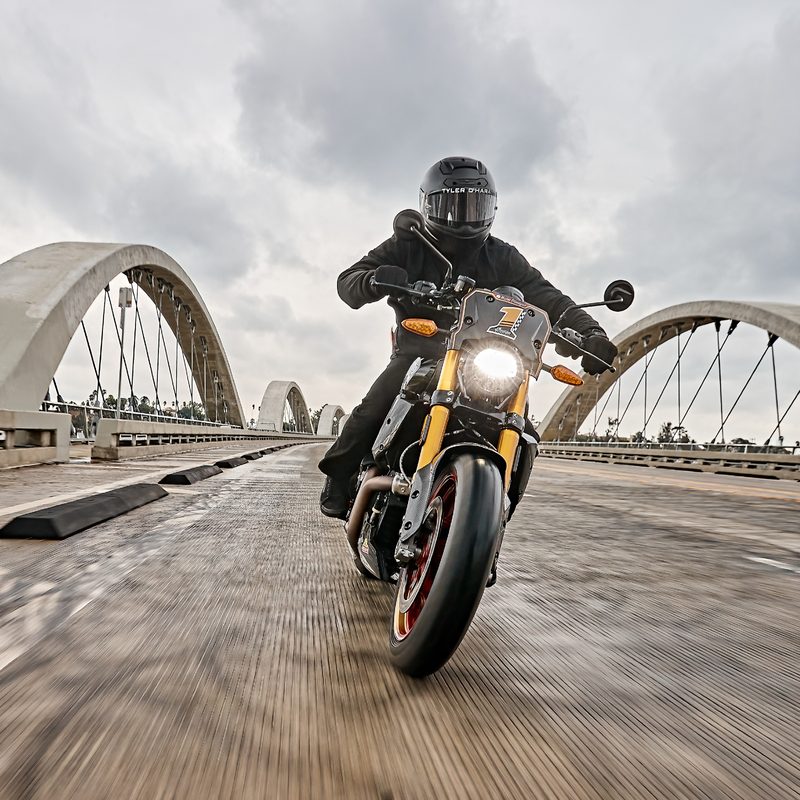 Rider wearing all black moto gear riding a 2024 Indian FTRxRSD Super Hooligan over a bridge.