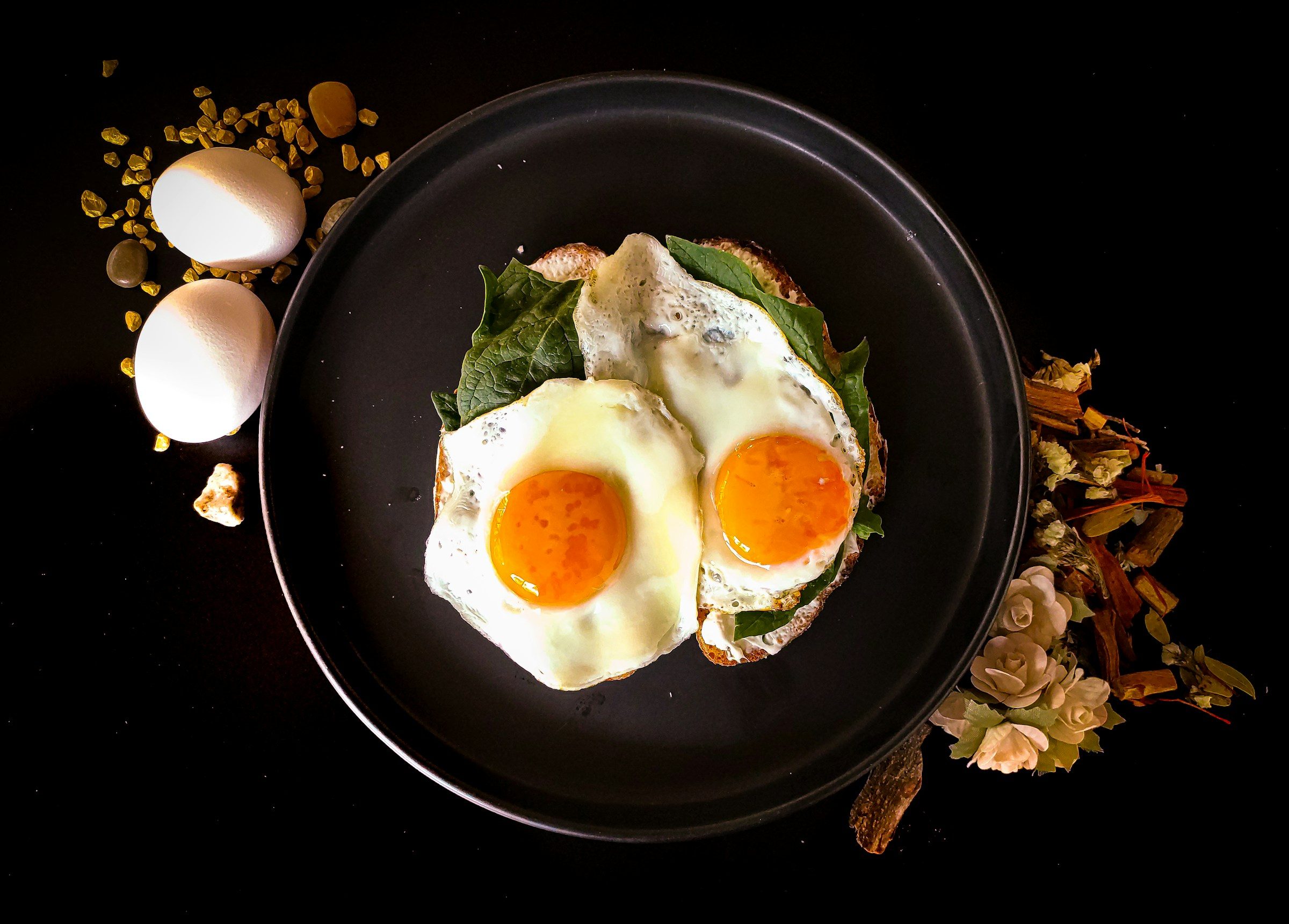 two fried eggs on a black plate with whole eggs in background on black table