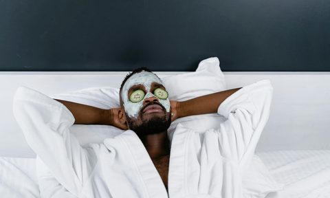 Man with white plush robe and cucumbers on his eyes