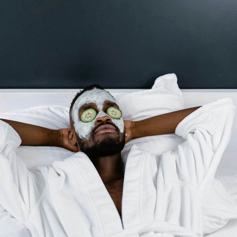 Man with white plush robe and cucumbers on his eyes