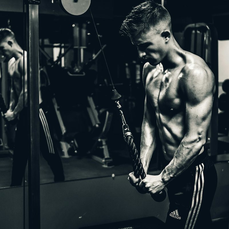 Black and white picture man shirtless doing cable pushdown exercise in the gym