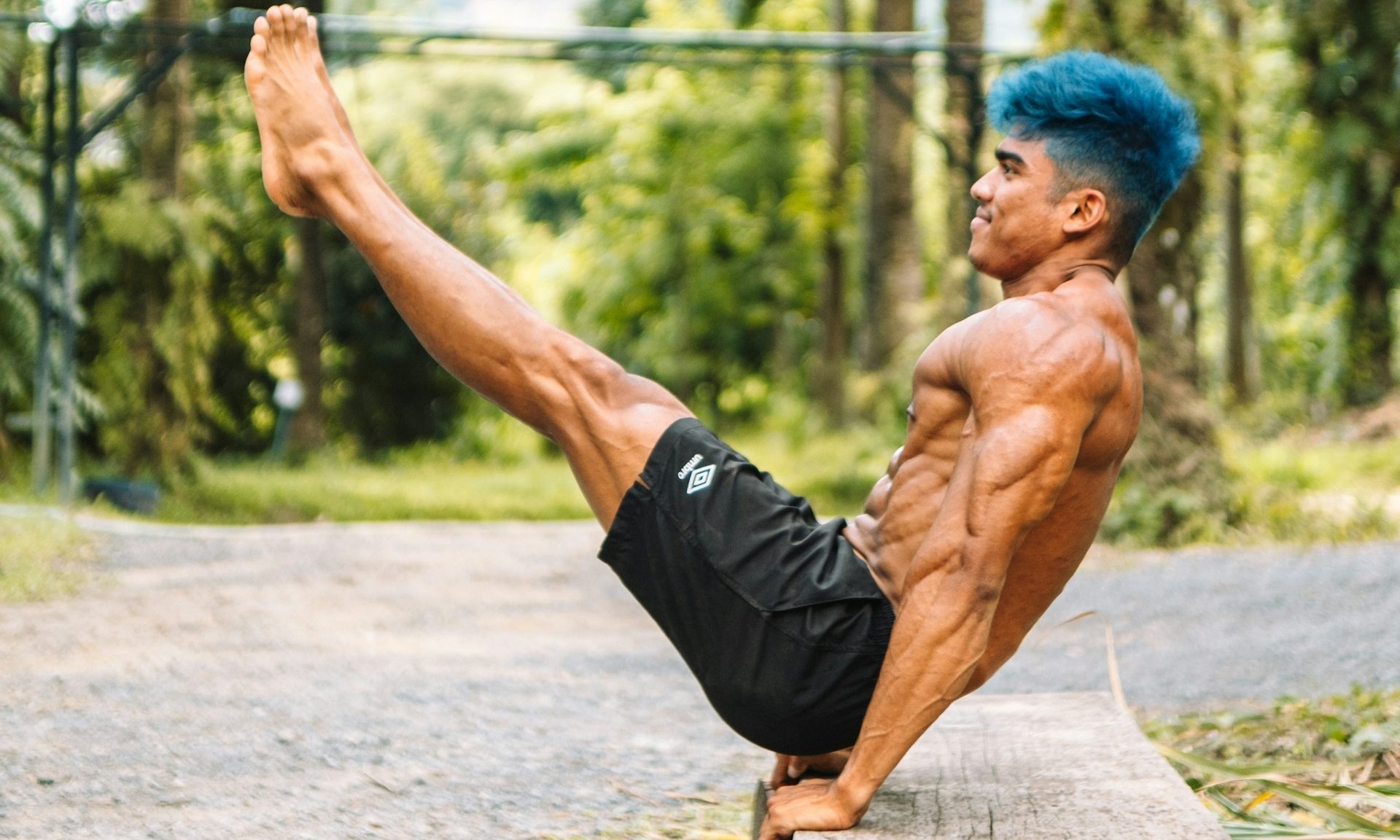 man blue hair exercising on a bench outside by the trees