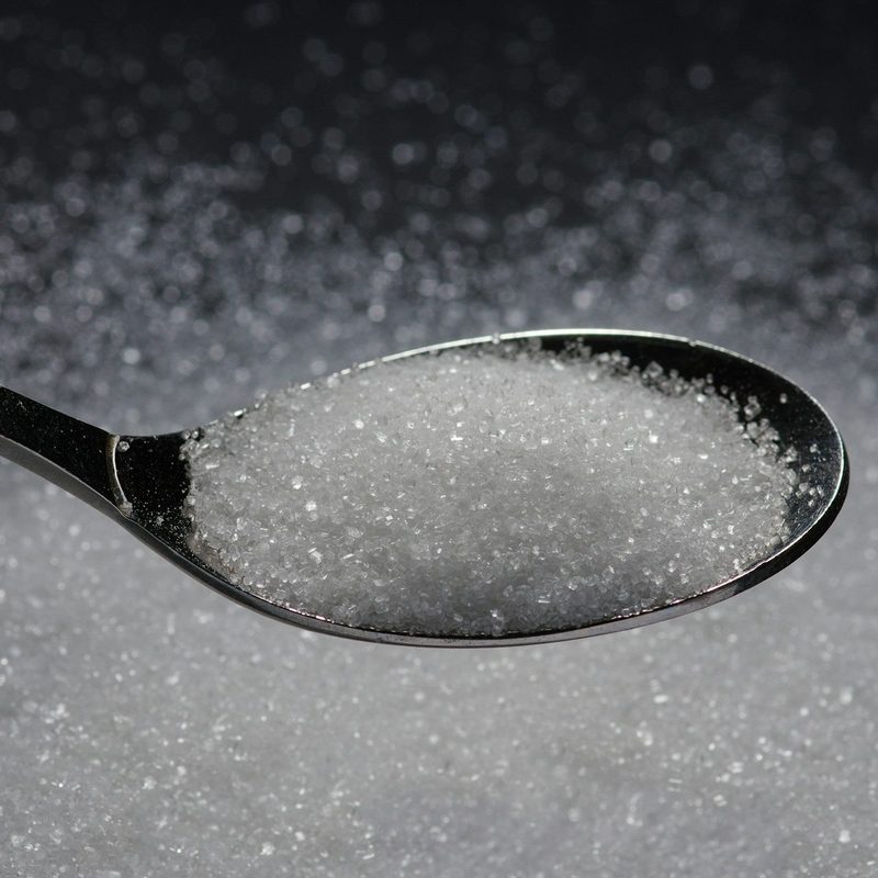 Spoonful of white sugar held above a dark table with white sugar on the table