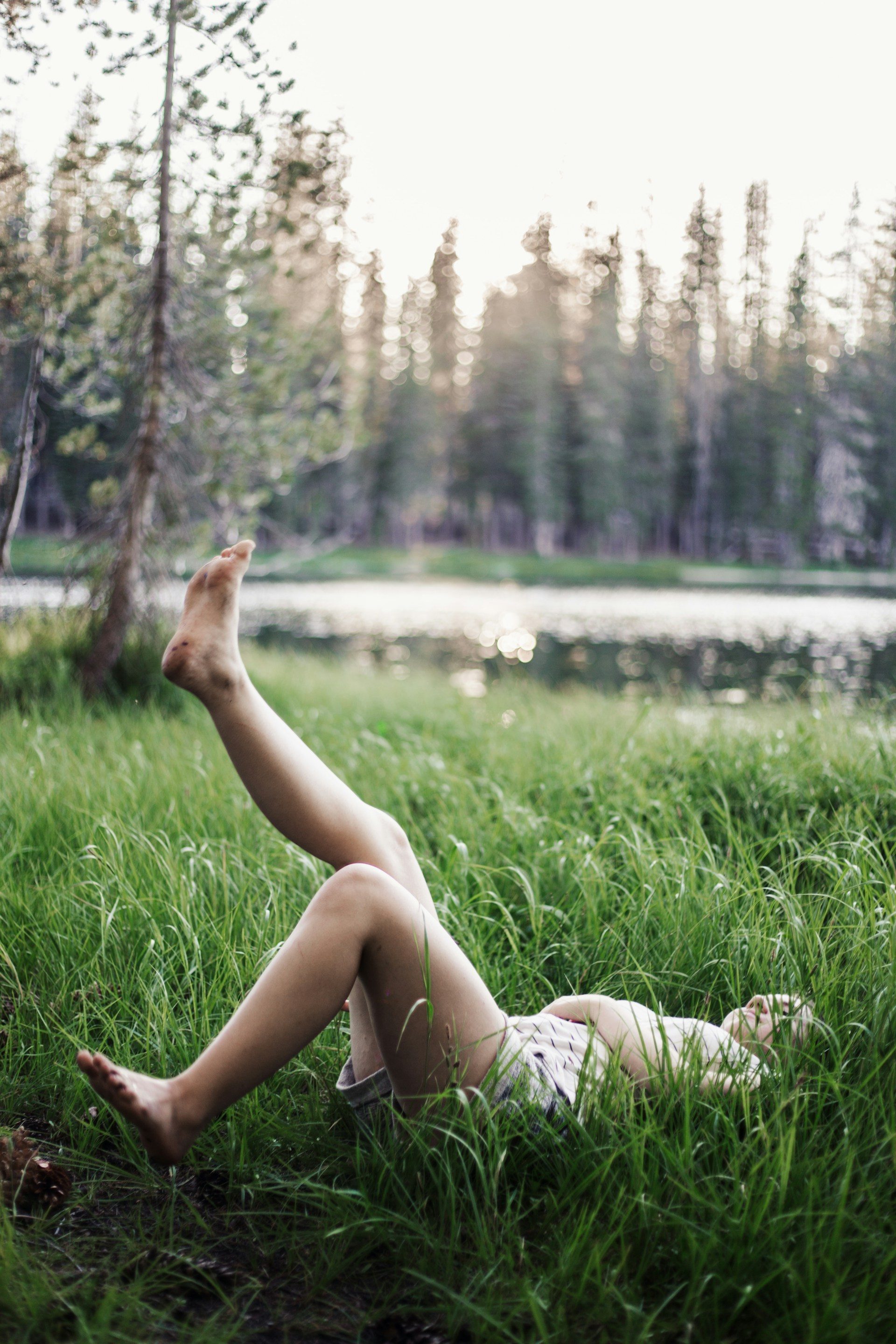 woman lying on back outside on the grass lifting legs in the air Pilates leg lift by the trees