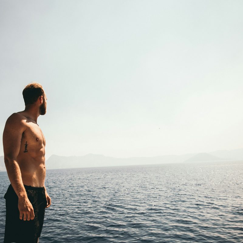 Shirtless man with strong abs at the beach looking at ocean
