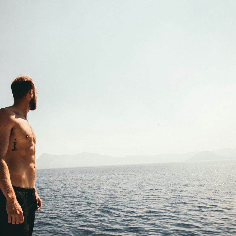 Man with shirt off and strong abs looking over the ocean