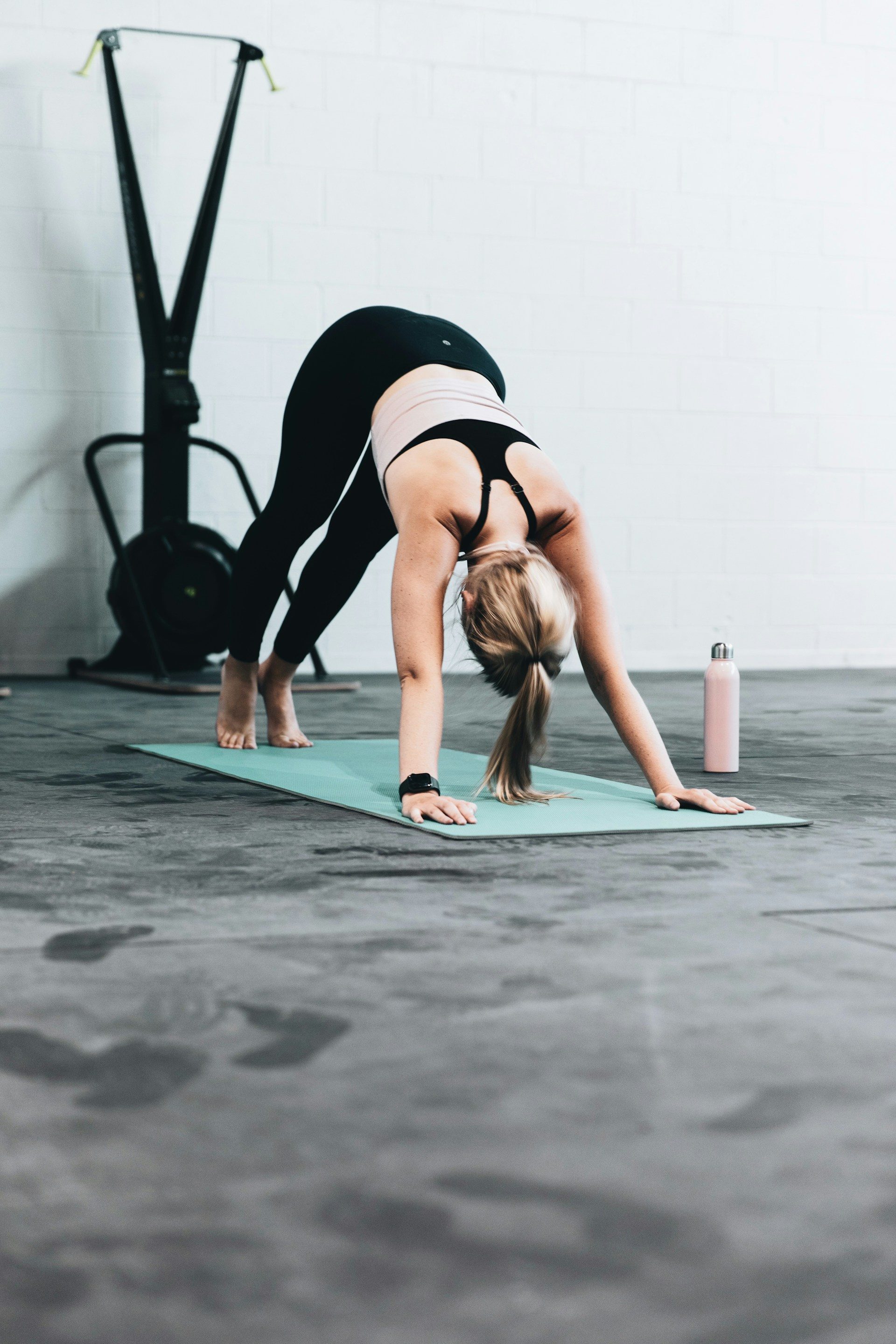 woman wearing gym clothes doing downward dog yoga pose on yoga mat in gym