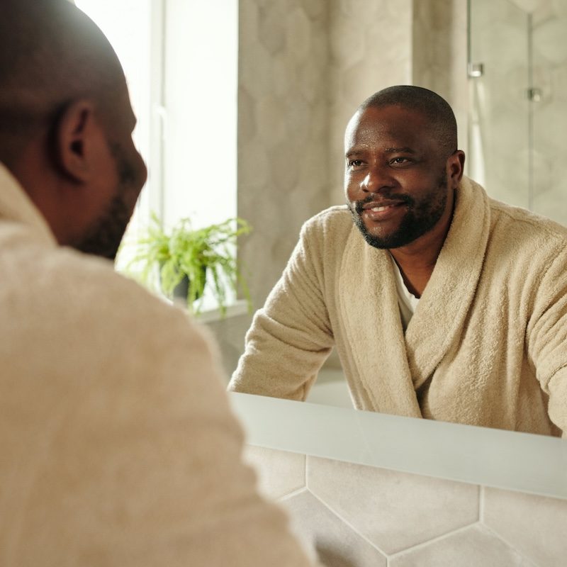 A man in a robe looking at his reflection in the mirror