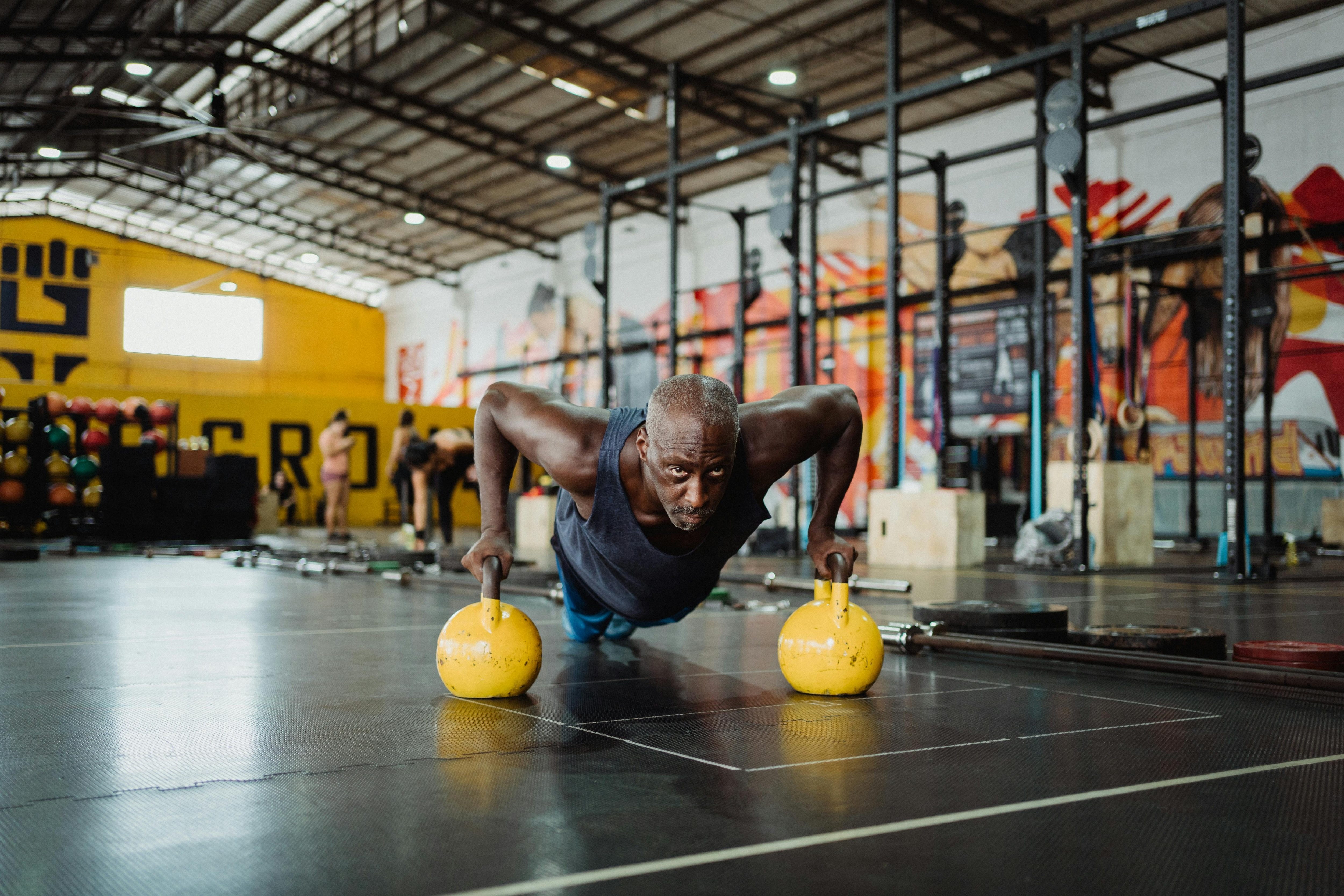 Man in gym doing pushup off of two kettle bells.