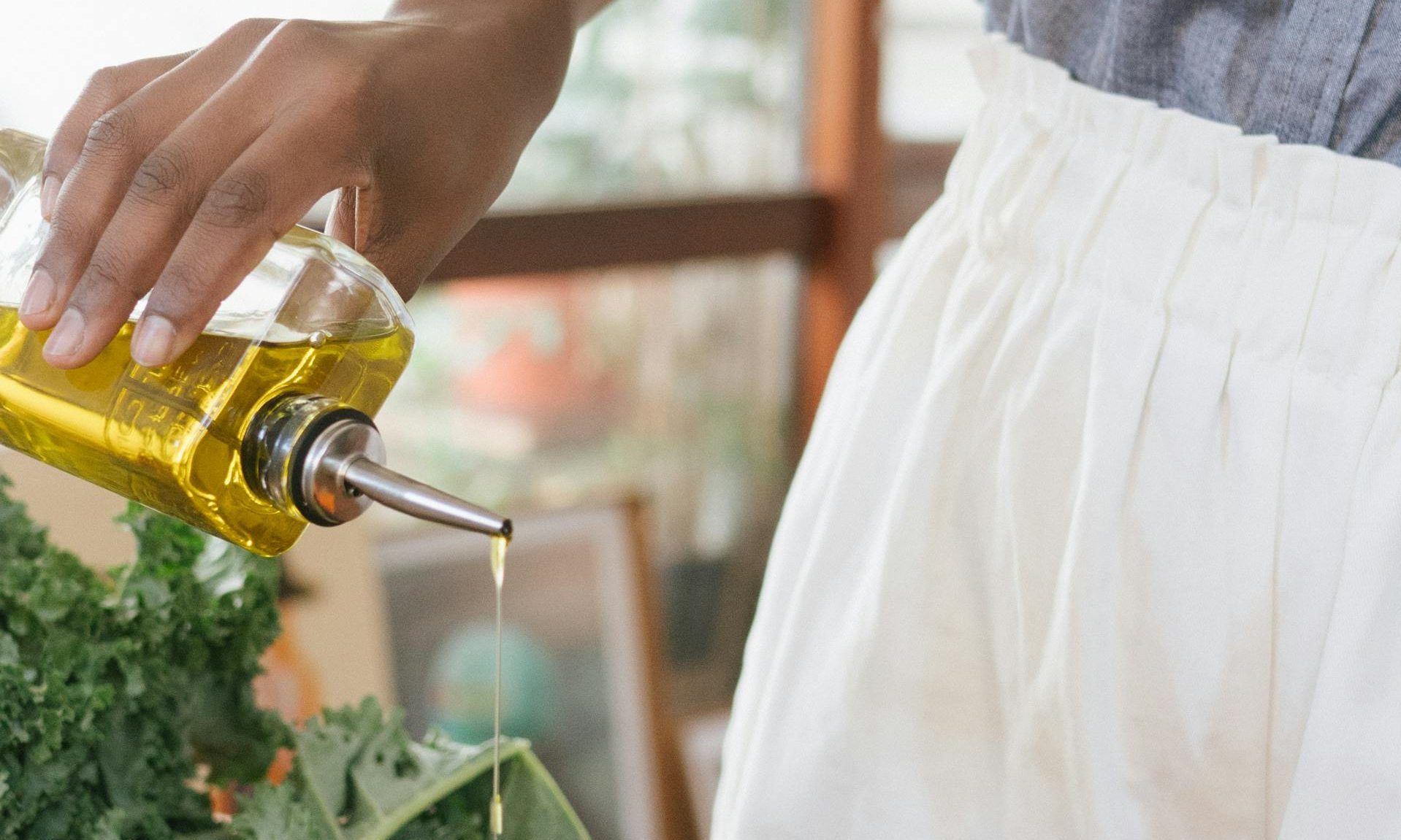Cooking pouring olive oil onto black pan with veggies and herbs on wooden table