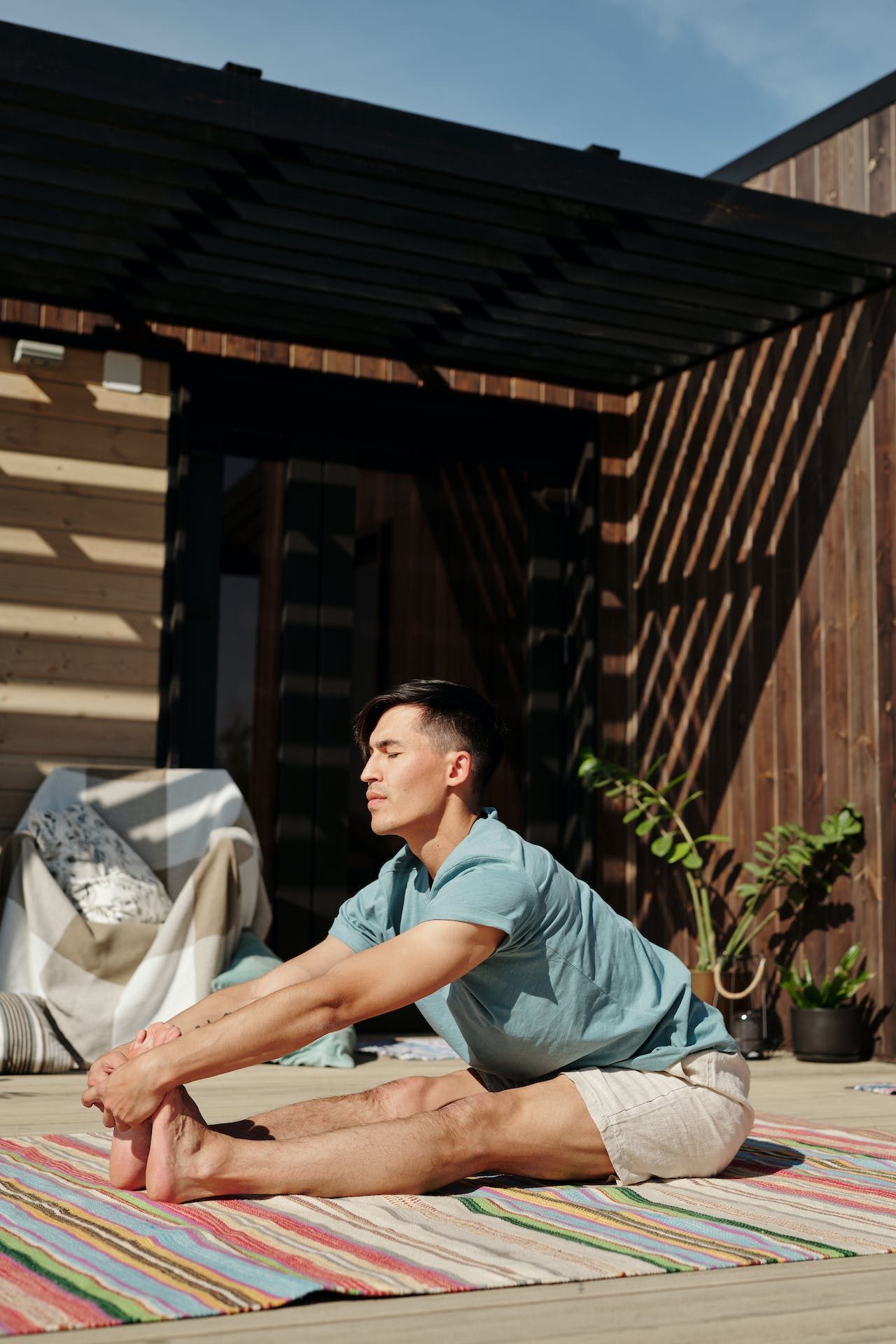 Man doing seated forward bend yoga pose outdoors on mat
