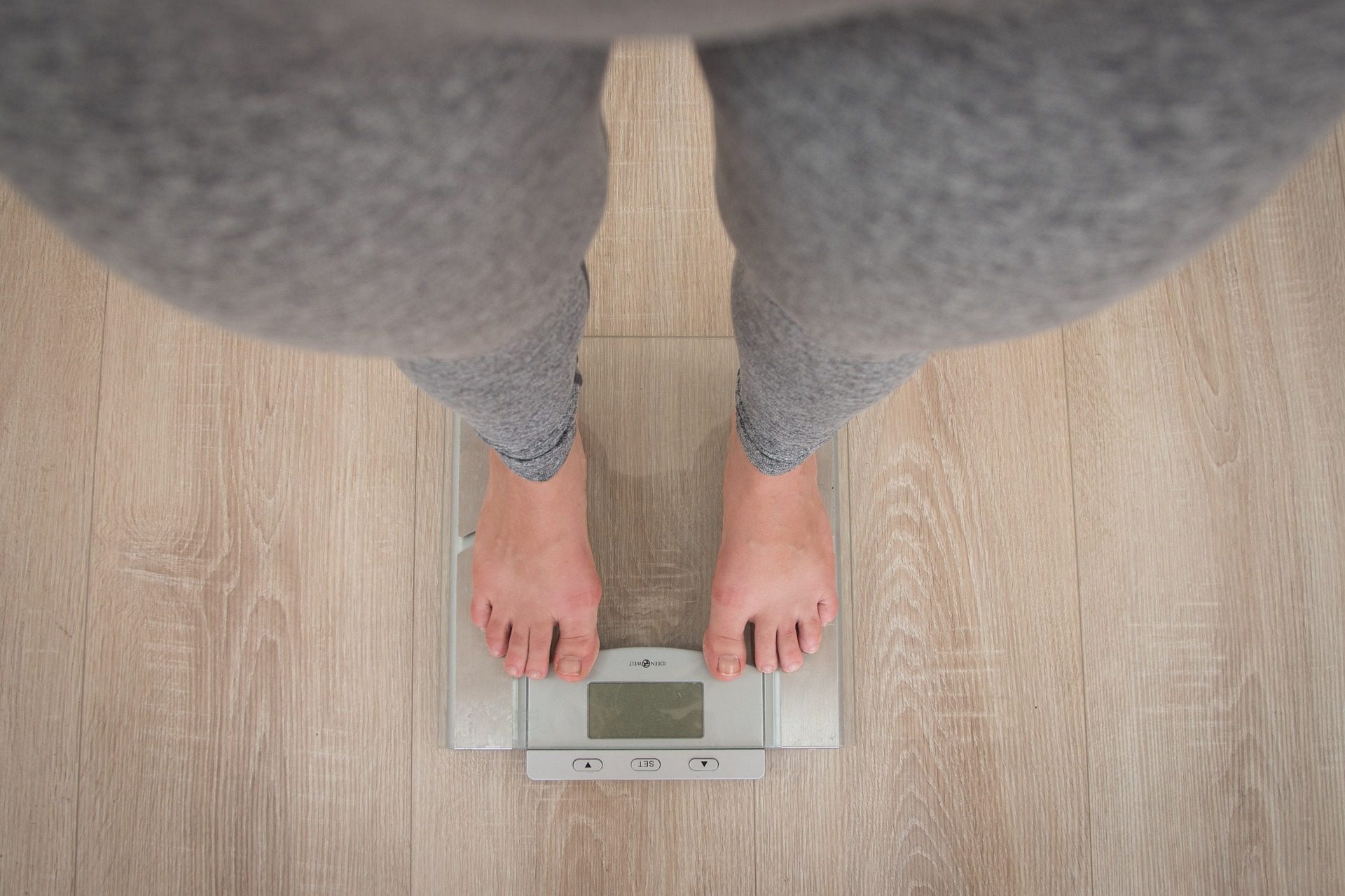 woman wearing grey leggings standing on weighing scale on wooden floor