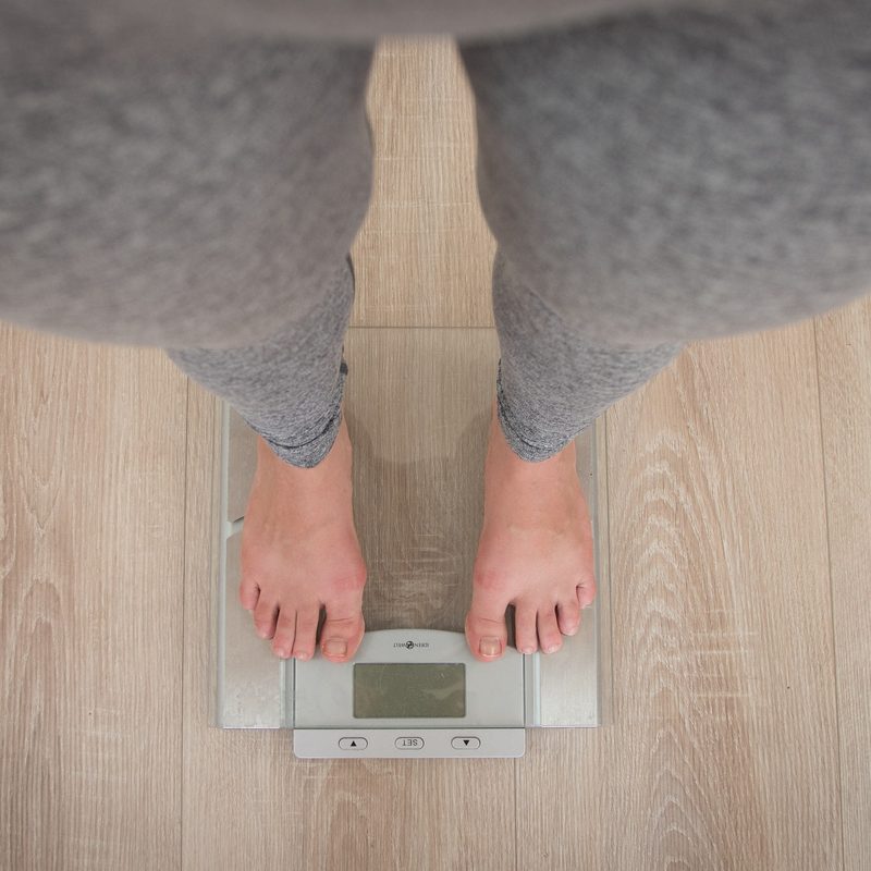 woman wearing grey leggings standing on weighing scale on wooden floor
