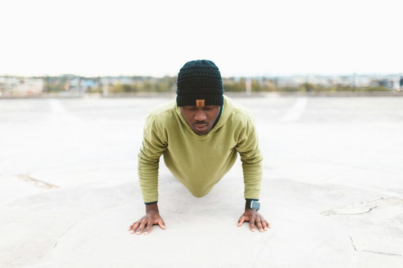 man wearing black hat and green shirt doing pushup or plank outside