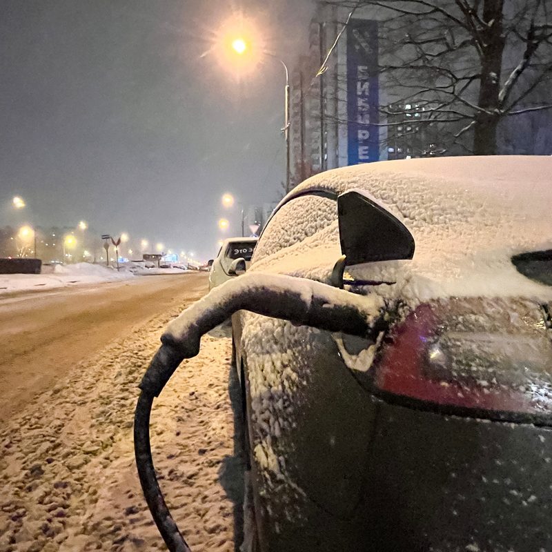 Electric car at night on city charging in snowdrifts. Tesla electric car charging in winter at night.