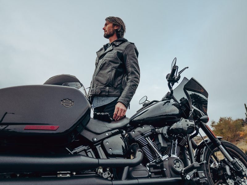 2024 Harley-Davidson Low Rider ST in Vivid Black color with rider standin.g next to the bike, both rained on