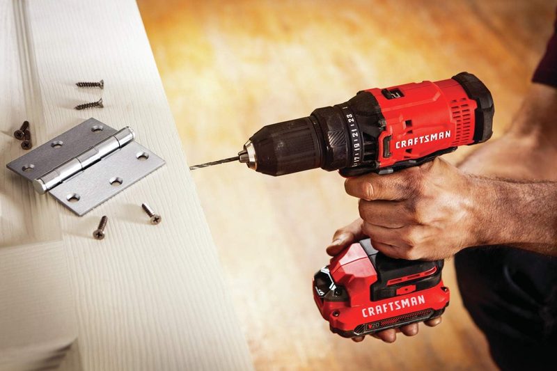 A man holds and steading the Craftsman V20 drill/driver to drill a hole into the side of a wooden door.