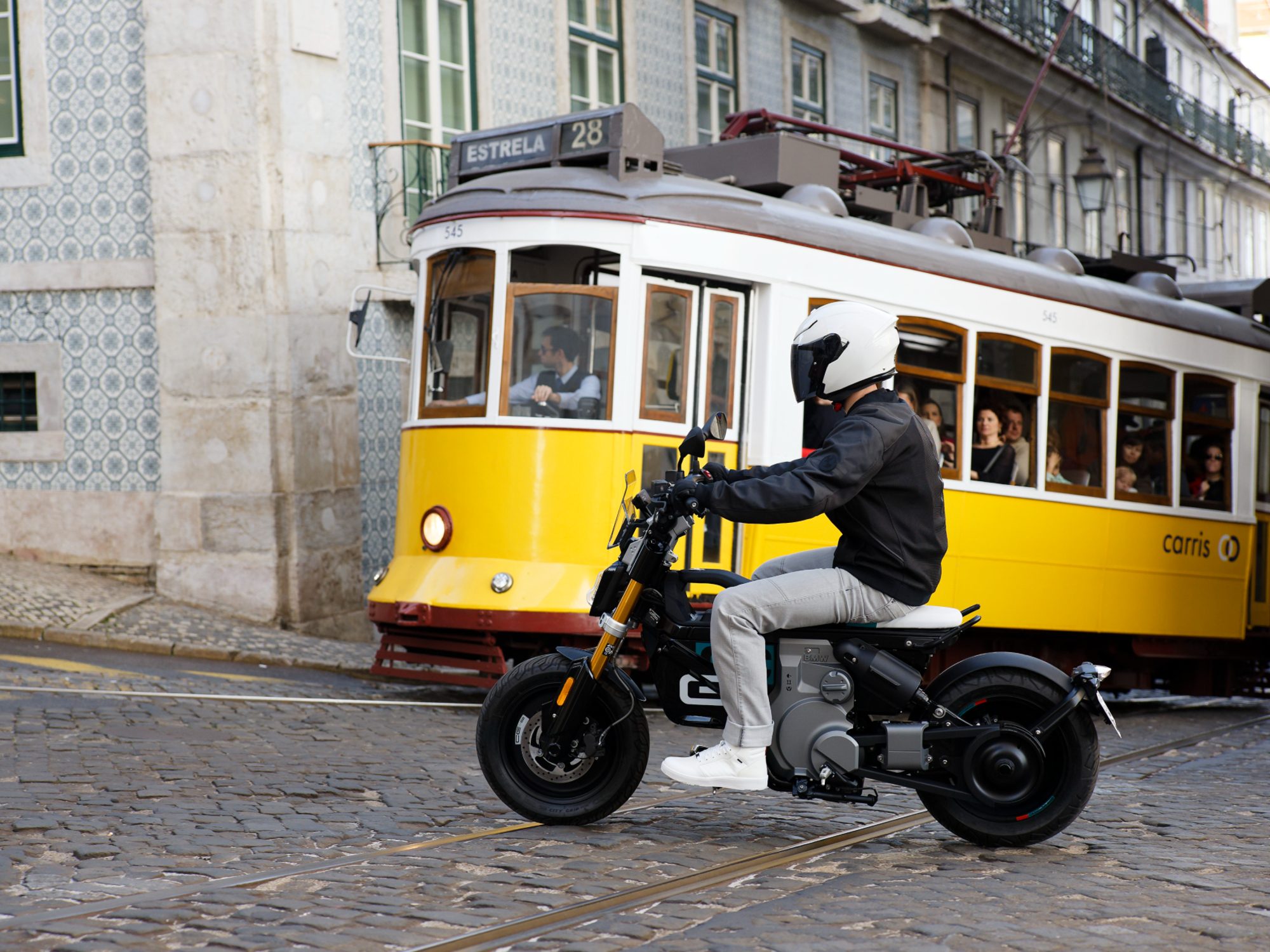 Helmeted rider on a 2024 BMW CE 02 traveling on a paved city about to cross street in front of a yellow streetcar.