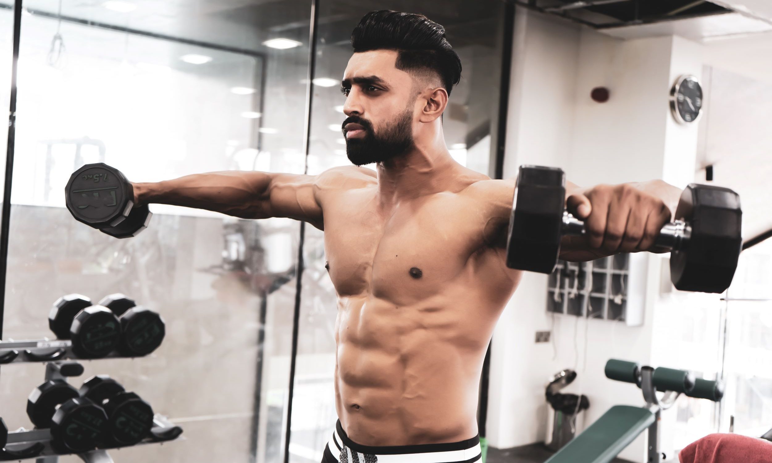 man shirtless weight lifting doing lateral raise with dumbbells at gym