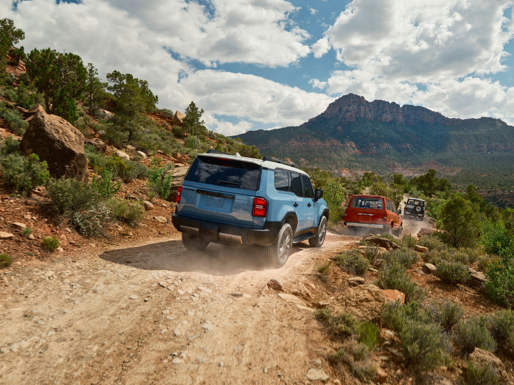 Three Toyota Land Cruisers of different vintages traveling down a rocky, desert road with a 2024 Toyota Land Cruiser trailing the others.