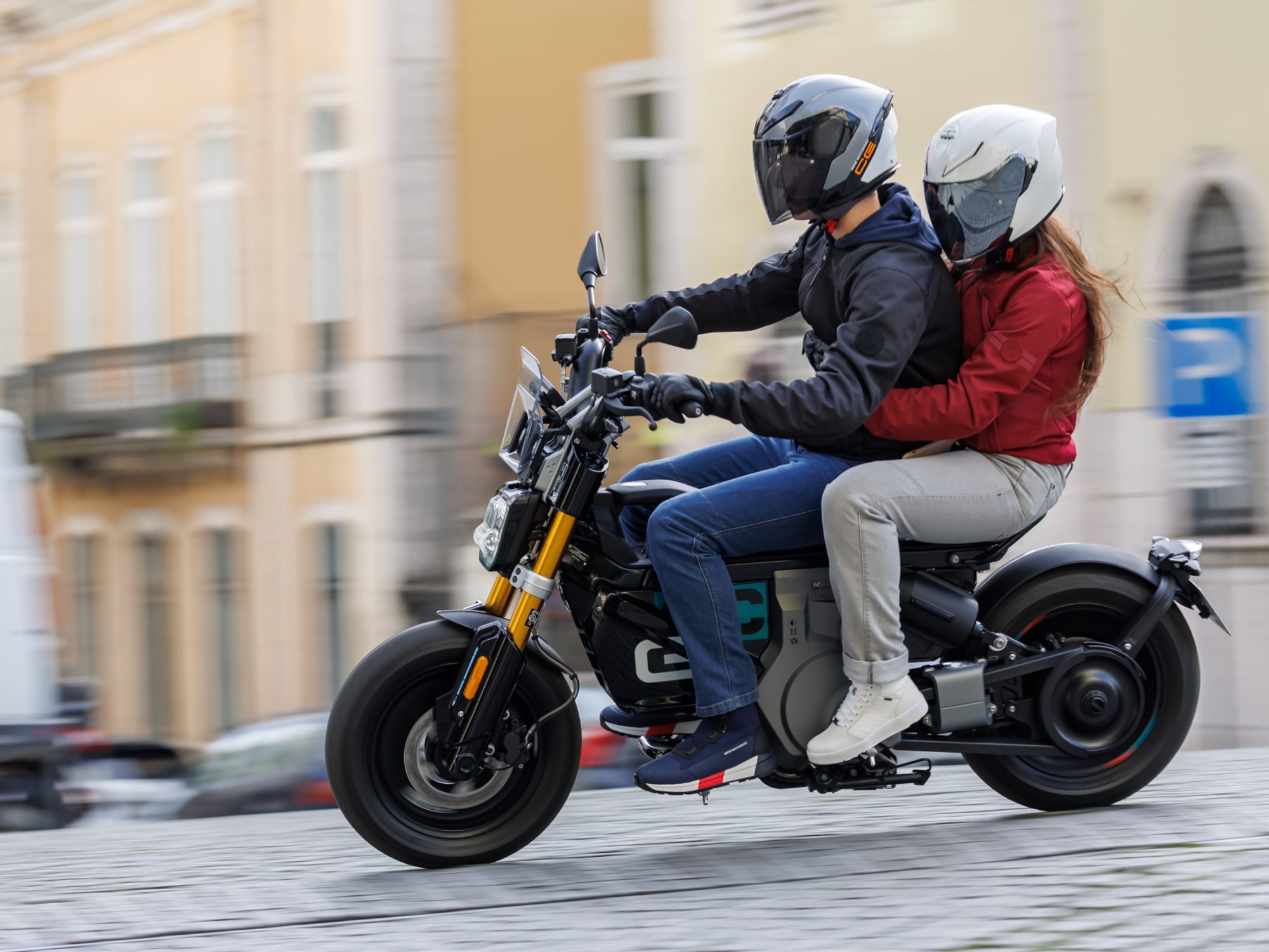 Two helmeted riders traveling on city street on a 2024 BMW CE 02