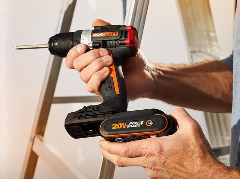 A man holds a Worx Nitro 20V WX130L drill driver, inserting one of the included Worx Powershare 20V batteries in the drill.