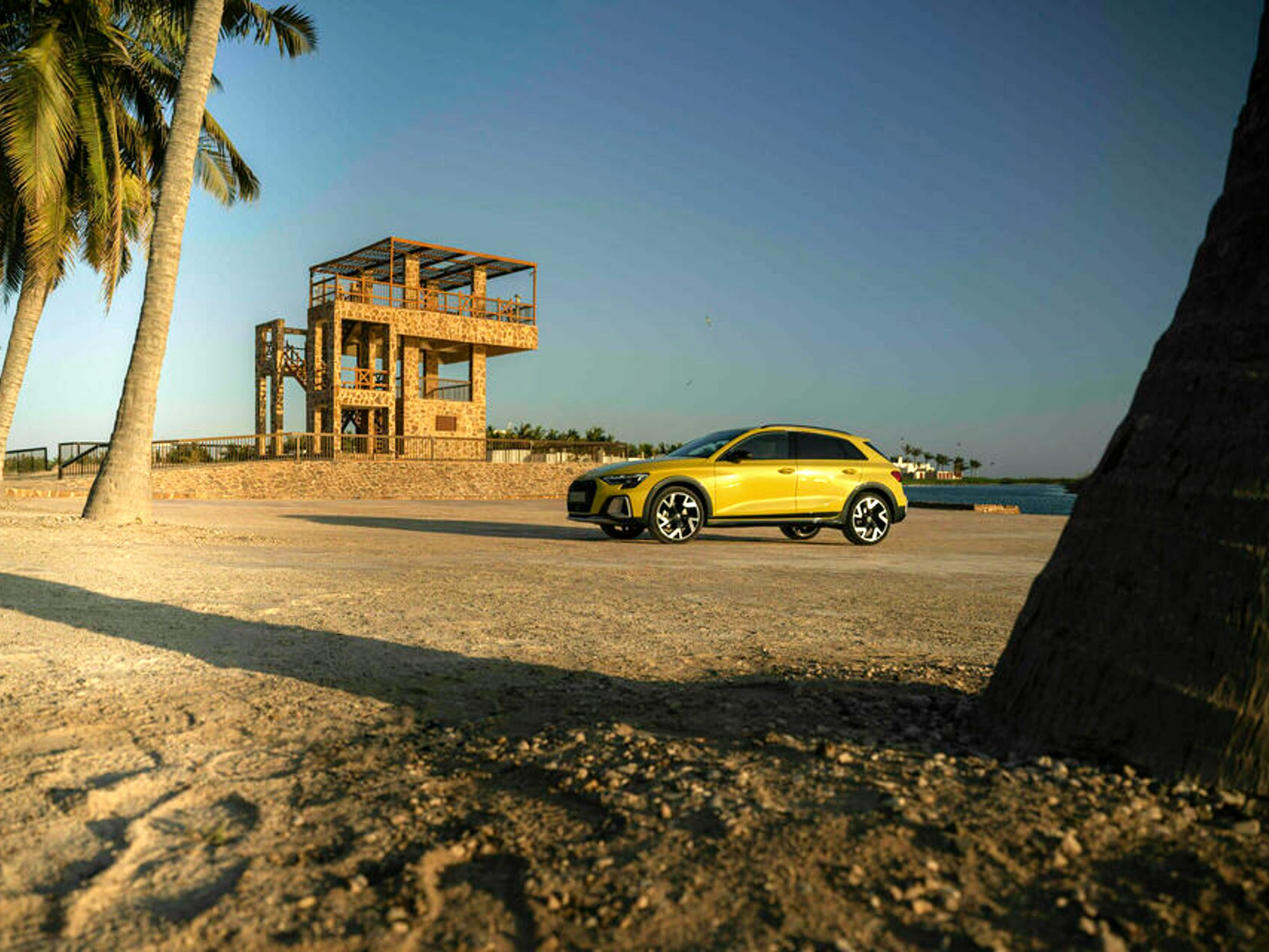 Yellow Audi A3 Allsteet parked on a beach with a lifeguard station and palm trees.