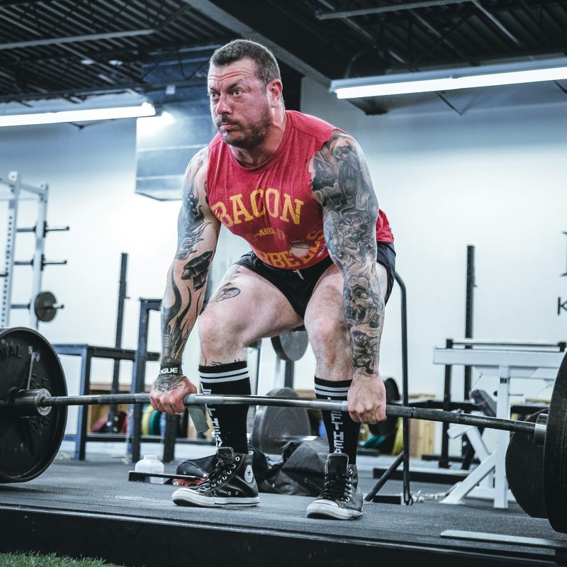 Man wearing red shirt and shorts in gym weight lifting dead lift man with tattoos