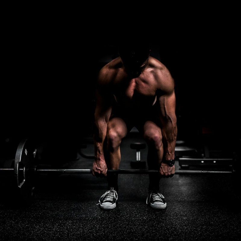 Shirtless man doing a deadlift weight lifting exercise with black background