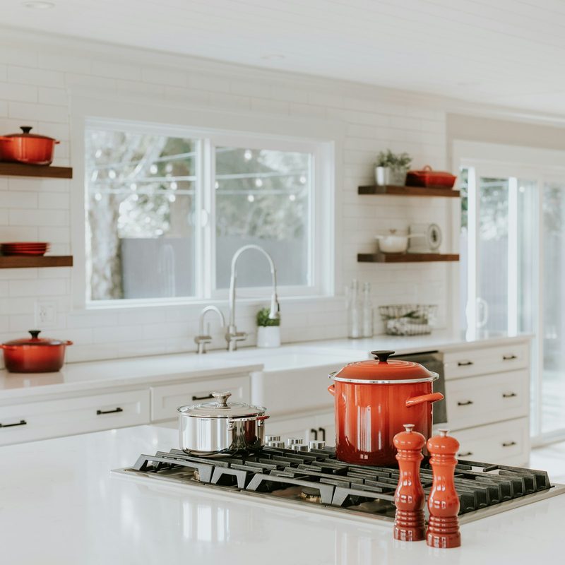 White modern large kitchen with red cookware and cooking pots and window and doors