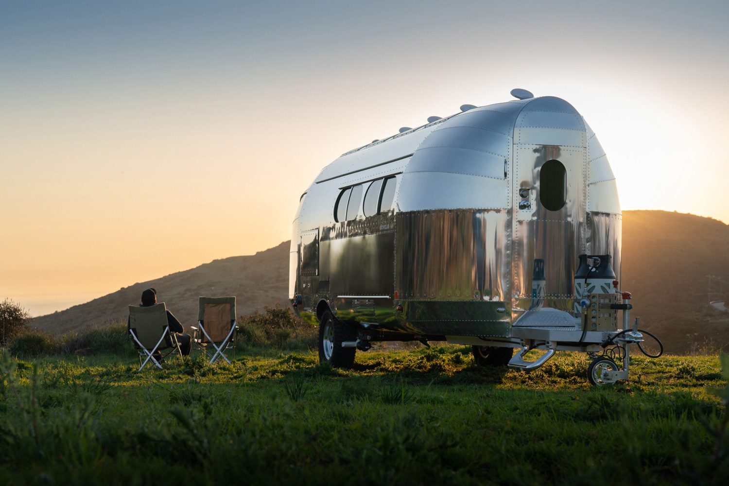 Bowlus Rivet travel trailer parked in a field with the sun in the background.