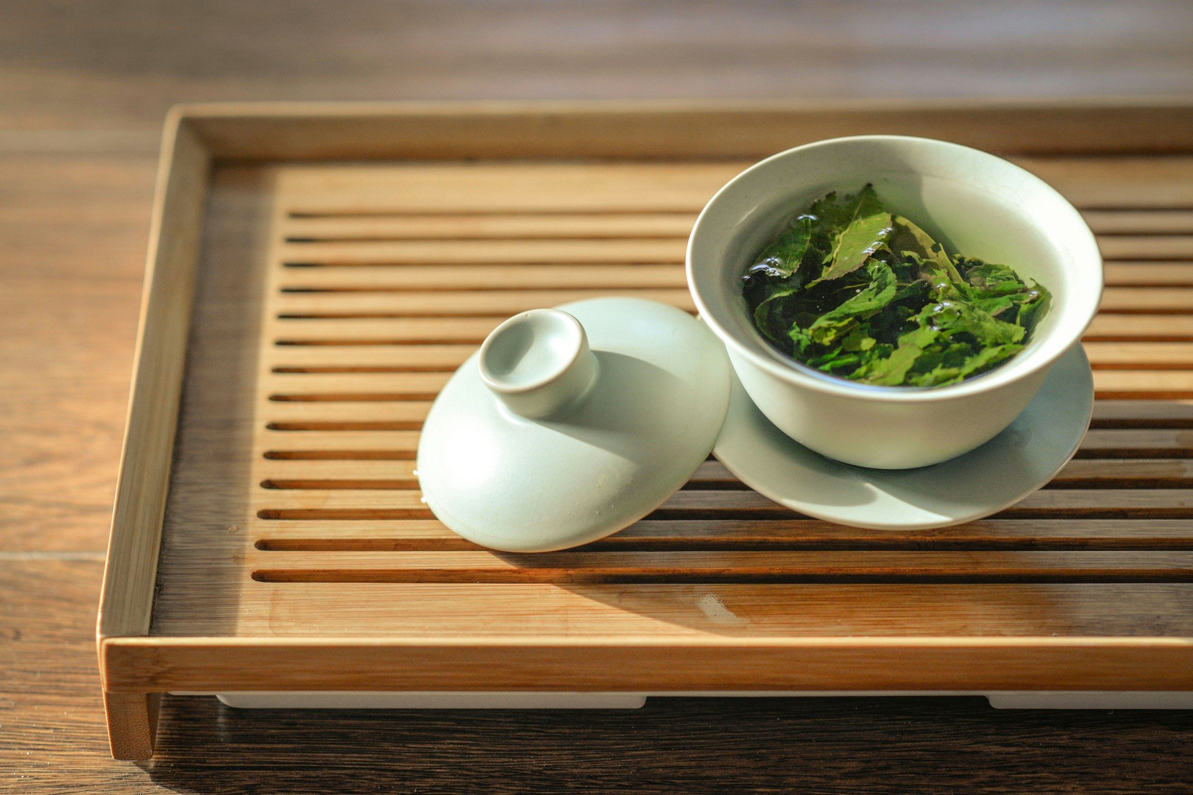 green tea leaves in a white bowl on a wooden tray on a wooden background