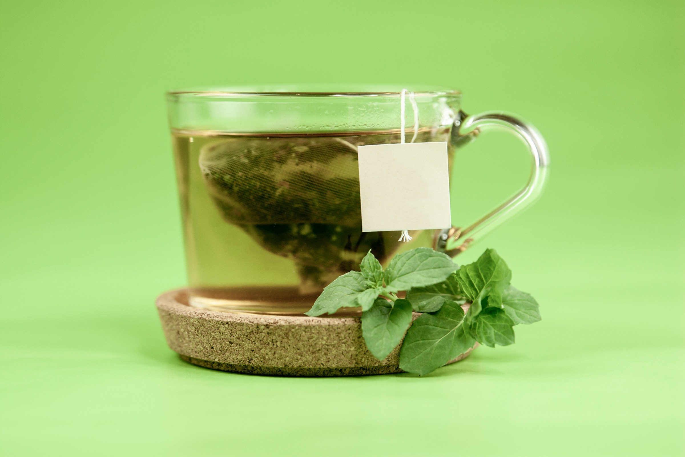clear glass cup of tea with green leaves and tea bag on green background