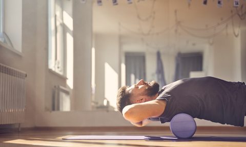 Handsome young man doing exercise with muscle therapy foam roller foam rolling on back