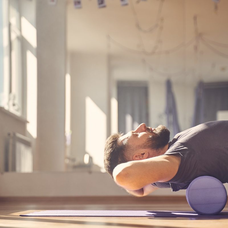 Handsome young man doing exercise with muscle therapy foam roller
