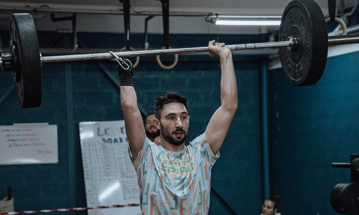 man in gym doing overhead press military press exercise wearing colorful shirt