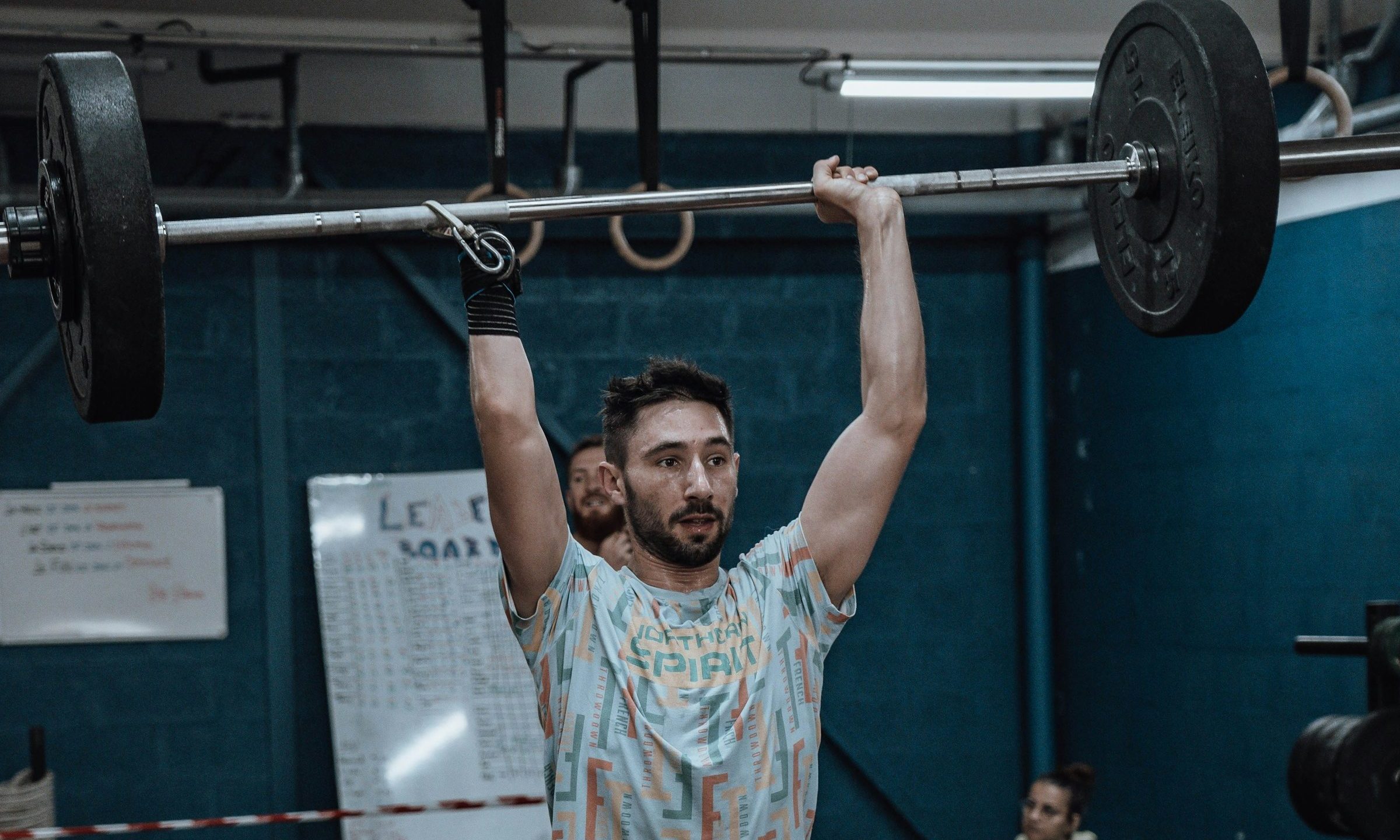 man in gym doing weight lifting overhead press wearing colorful shirt