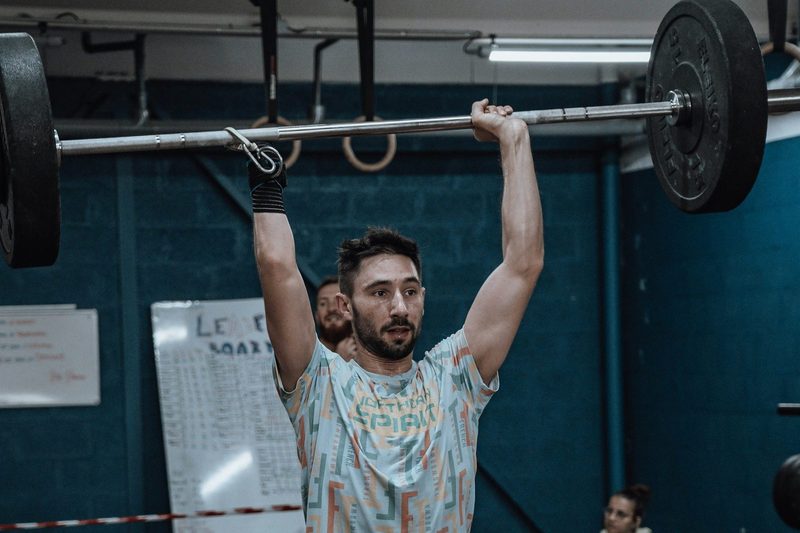 man in gym doing overhead press military press exercise wearing colorful shirt