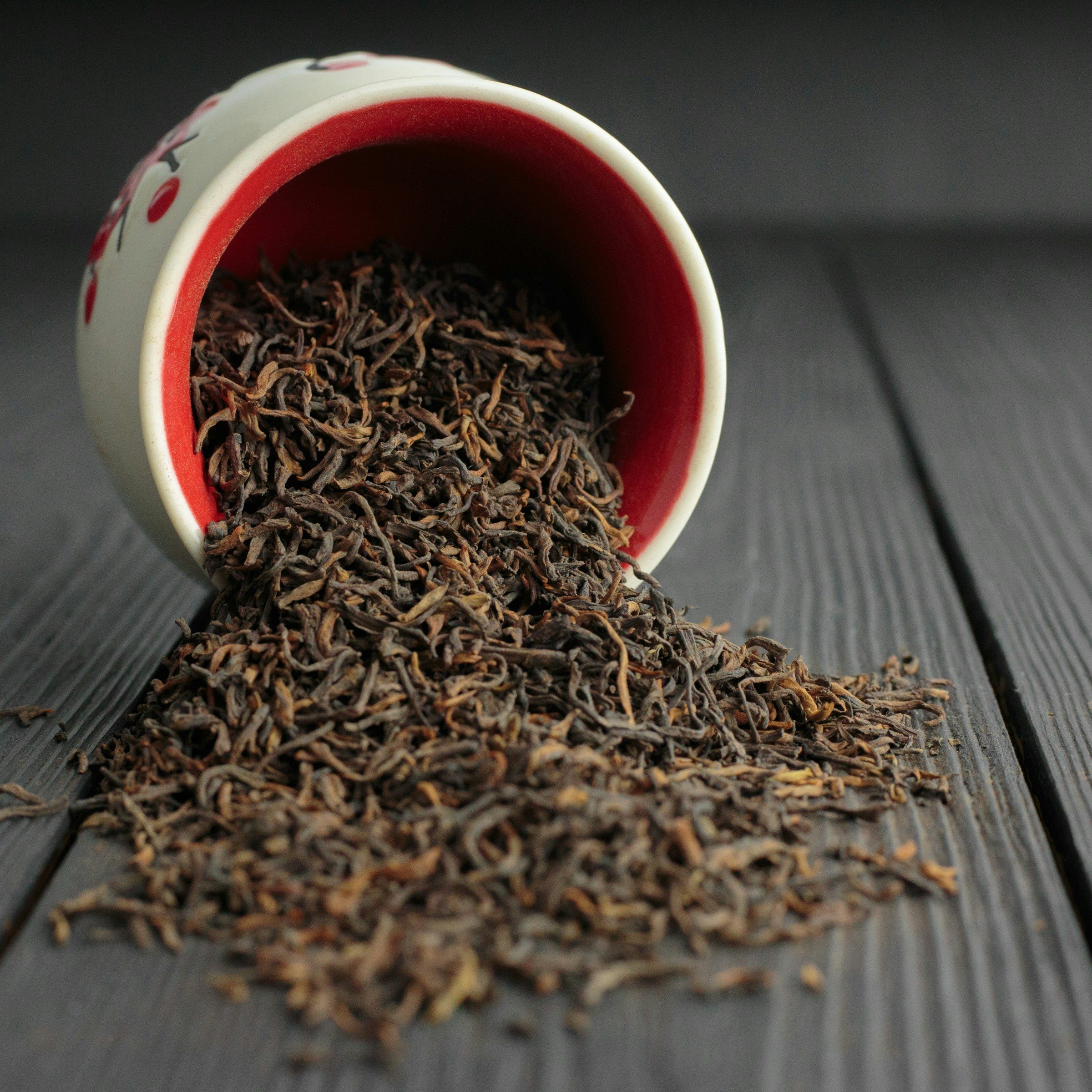 black tea leaves spilling out from white and red ceramic jar onto dark wooden table