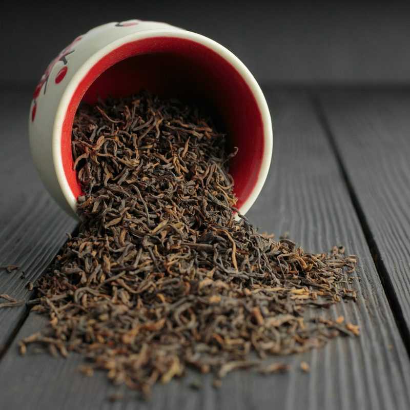 Black tea leaves spilling out from white and red ceramic jar onto dark wooden table