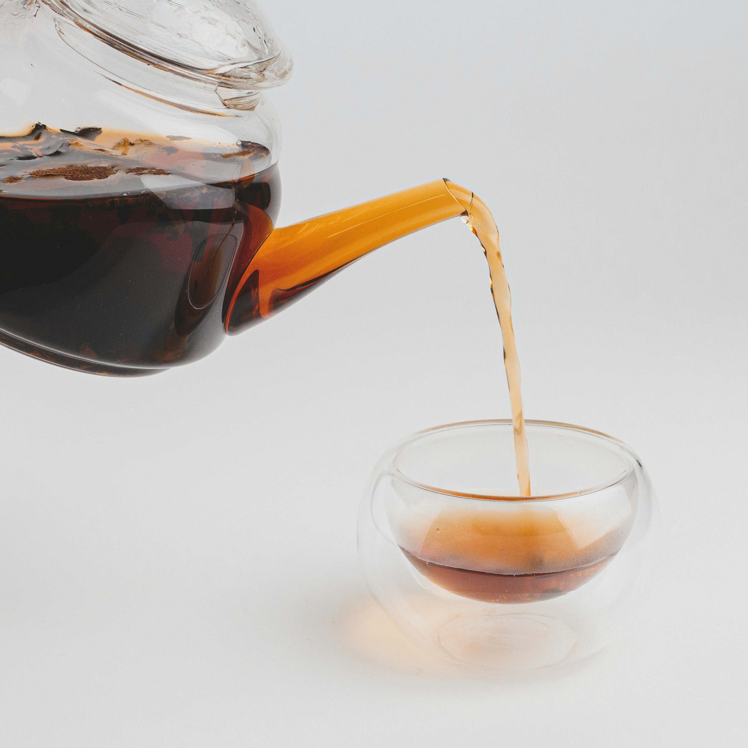 Glass teapot pouring black tea into a small glass cup