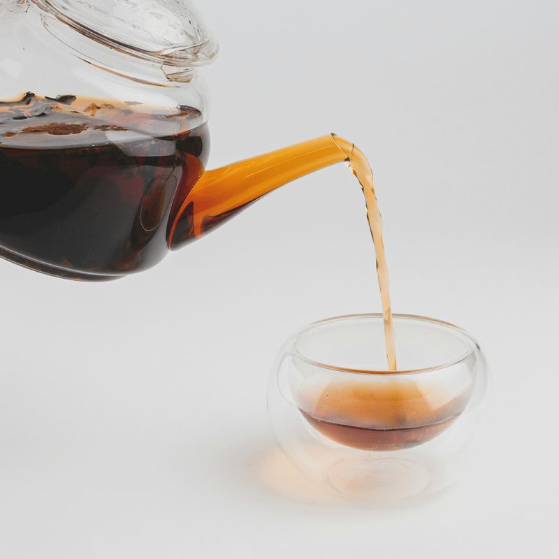 Glass teapot pouring black tea into a small glass cup